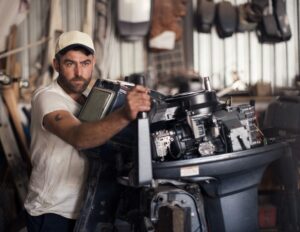 Man working on an outboard motor in a marine repair shop, showcasing expertise in boat maintenance and repair services offered by Mike & Dave's Pro Marine.