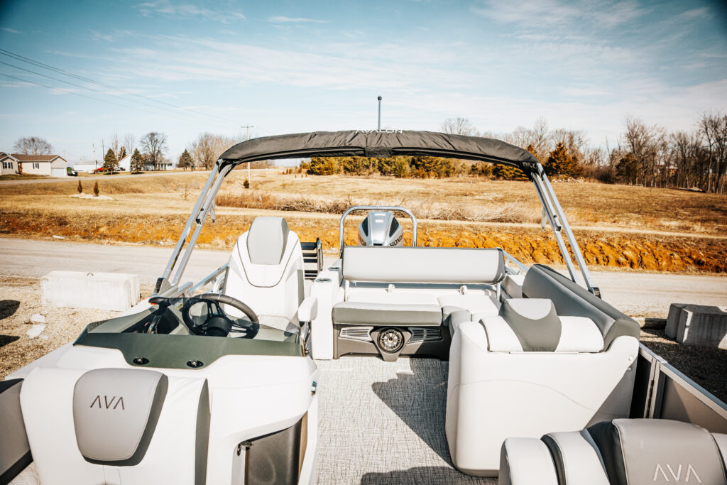 2026 Avalon LSZ (White) boat interior featuring a versatile rear bench, helm with steering wheel, and plush seating in charcoal and white vinyl, set against a scenic outdoor backdrop.