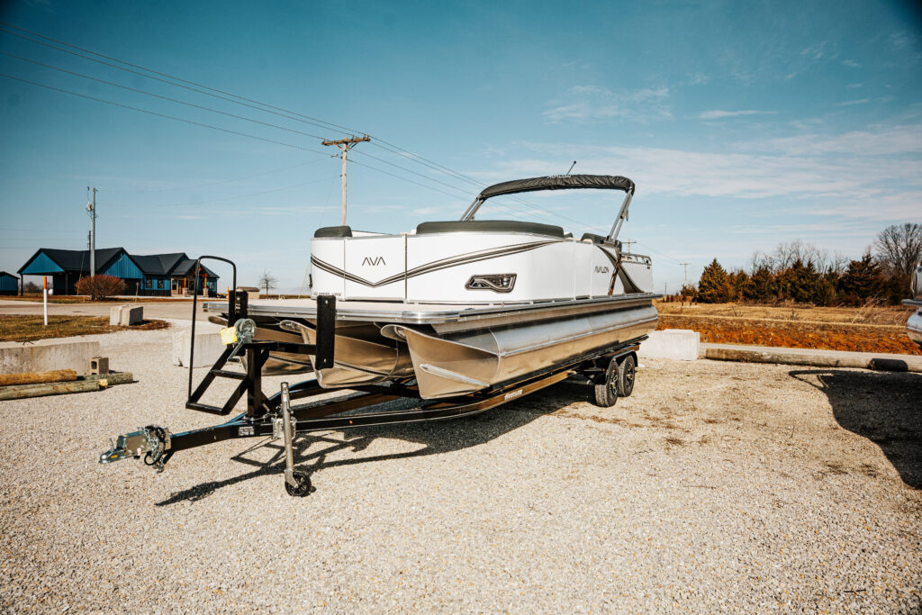 2026 Avalon LSZ boat on trailer, showcasing sleek white design and modern features, set against a clear blue sky and gravel lot.