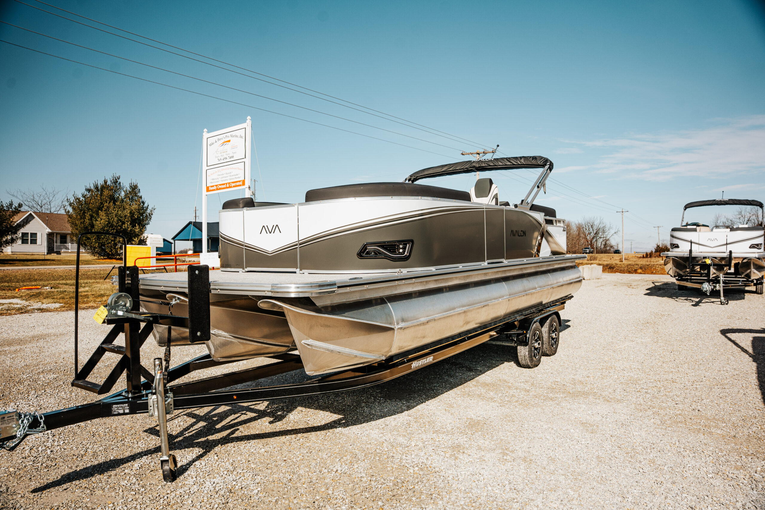 2026 Avalon LSZ pontoon boat in black and silver parked on a trailer at Mike & Dave's Pro Marine, showcasing a sunny outdoor setting with nearby marine inventory.