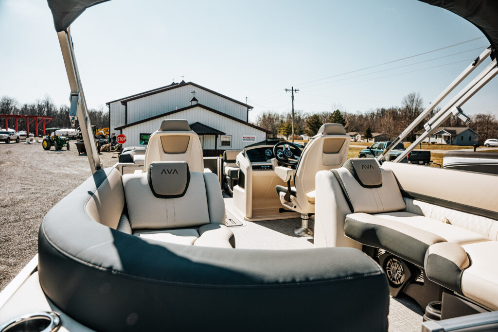 Interior view of the 2026 Avalon Catalina Quad Lounger in Matte Black, showcasing plush seating with Avalon branding, modern helm controls, and a scenic outdoor backdrop.