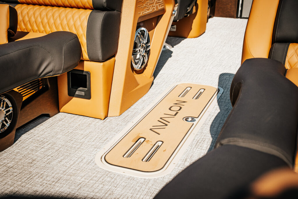 Interior view of the 2026 Avalon Catalina boat featuring plush seating in black and cognac, Avalon logo on the floor, and stylish audio speakers.