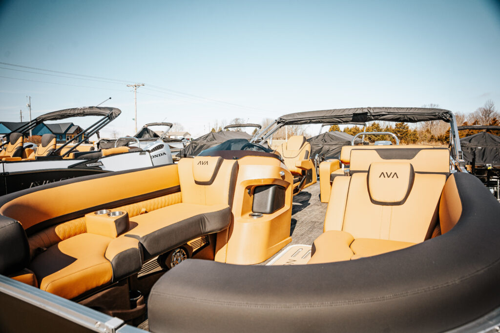 Interior view of 2026 Avalon LSZ boat showcasing luxurious seating with black and cream vinyl upholstery, featuring the Avalon logo, surrounded by additional boats in a marina setting.