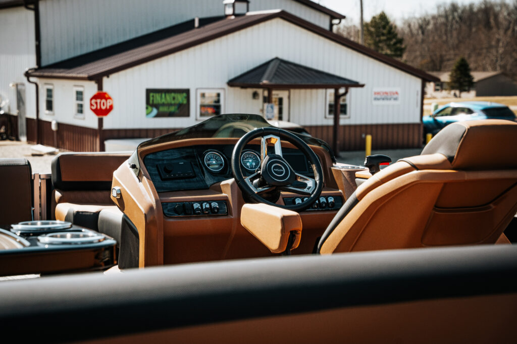 Interior view of the 2026 Avalon LSZ boat showcasing the helm with steering wheel, control panel, and plush seating, with a financing sign visible in the background.