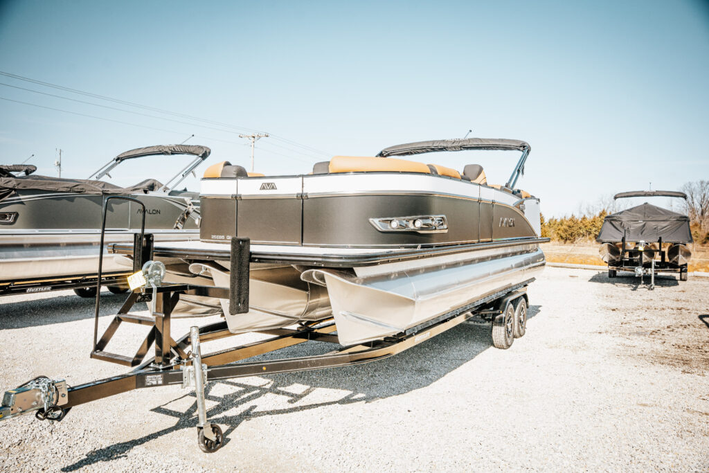 2026 Avalon LSZ Entertainer pontoon boat on trailer, showcasing sleek design with black and silver accents, parked among other boats in a marine sales lot.