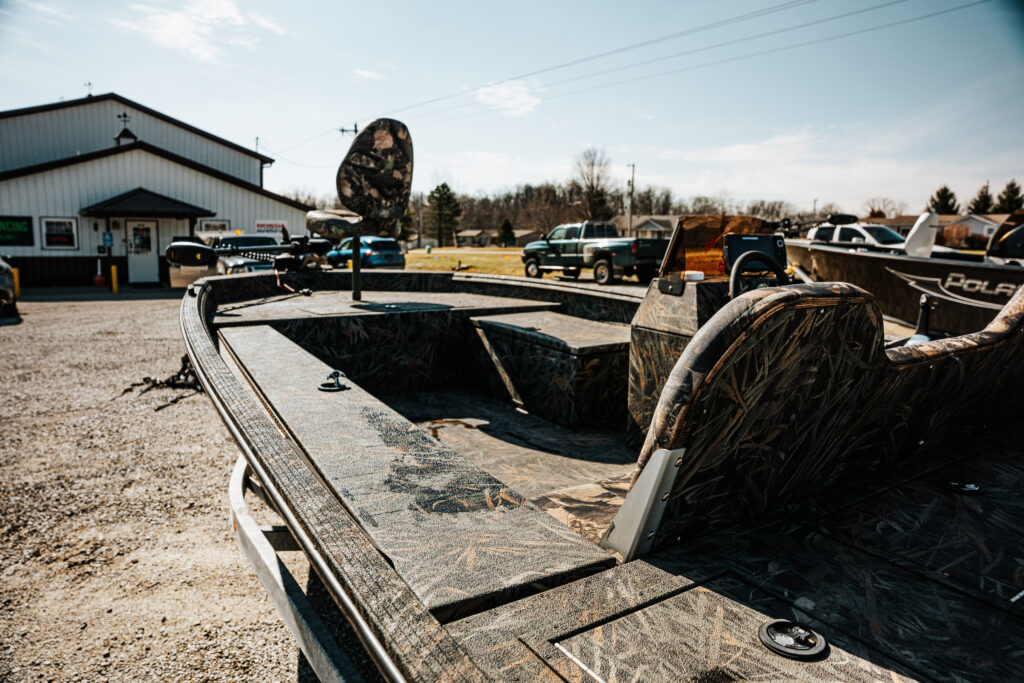 2024 Polar Kraft Sport X 190 SC boat interior featuring upgraded fishing seats, bench seat, and camouflage pattern, with a dealership in the background.