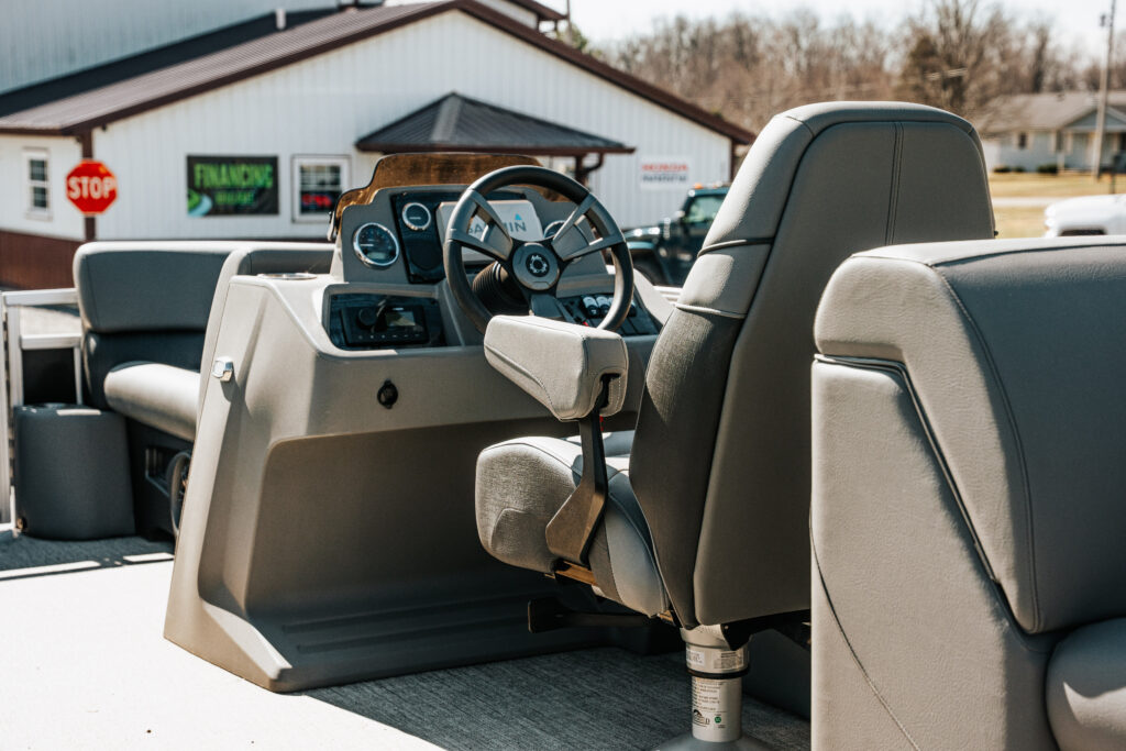 Avalon Venture Quad Lounger boat interior featuring a reclining commander's chair, steering wheel, and control panel, with a backdrop of a financing sign.