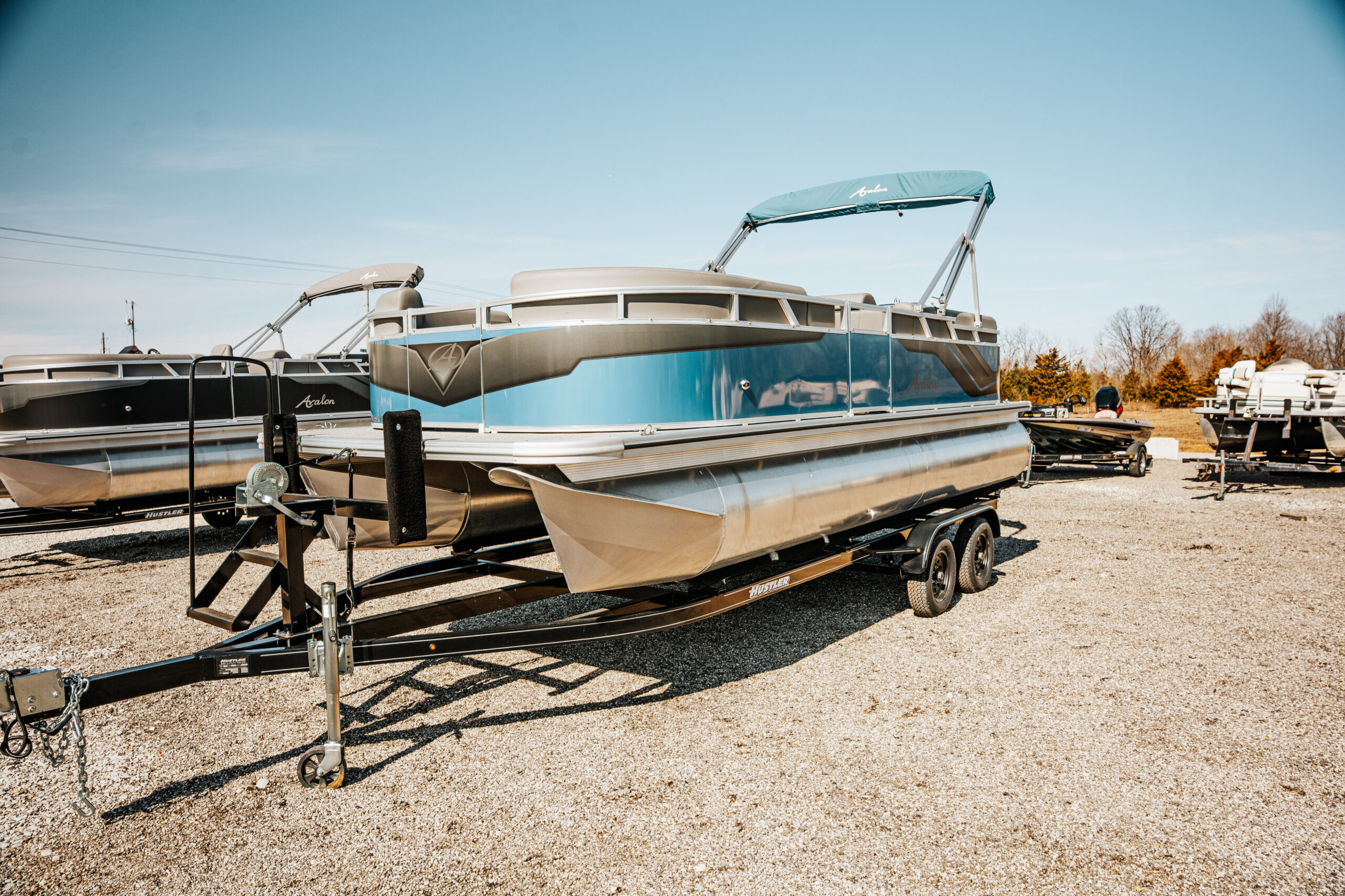 Avalon Venture Quad Lounger boat in blue color on a trailer, surrounded by other boats in a marine inventory setting.