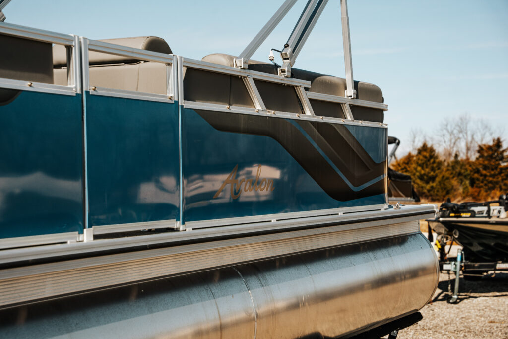 Avalon branding on the side of a 2024 Avalon Venture Quad Lounger boat with blue and black matte finish, showcasing seating and design features.