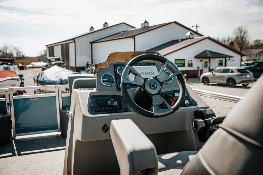 Boat cockpit view featuring Garmin display and steering wheel, showcasing the interior of the 2024 Avalon Venture Quad Lounger (Blue) in a marina setting.